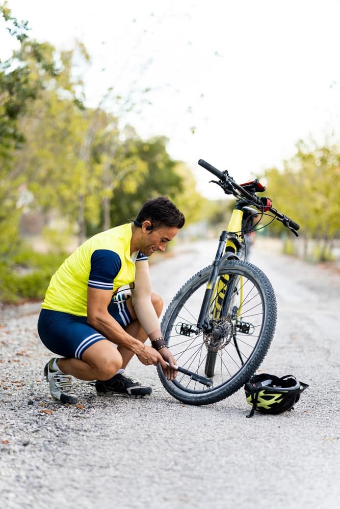 A person with a prosthetic arm, wearing sports attire, crouches to inflate a mountain bike tire with an air pump.