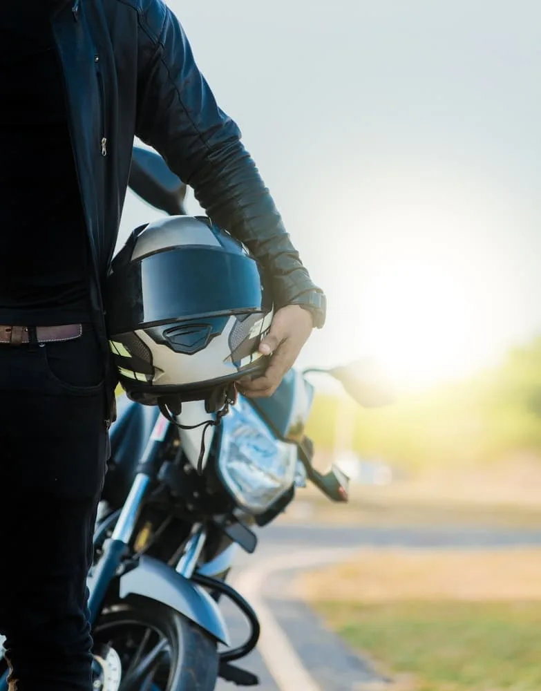 Unrecognizable motorcyclist holding a safety helmet next to his bike by the road, emphasizing motorcycle safety.