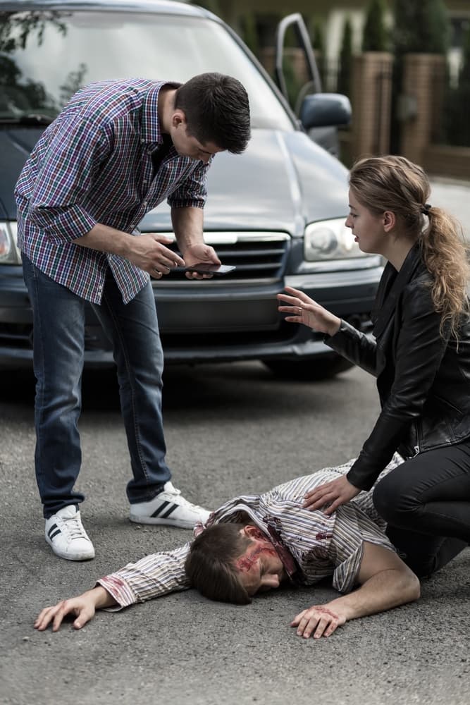 People providing first aid to individual involved in a car collision.