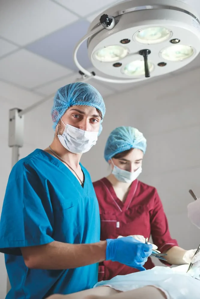 Surgeons in uniform operating, focused on the task, looking at the camera.