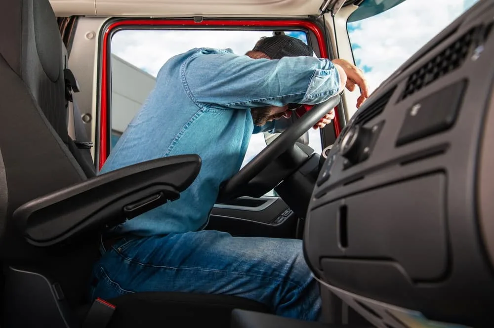 Exhausted truck driver rests on steering wheel in vehicle cabin after finishing route.