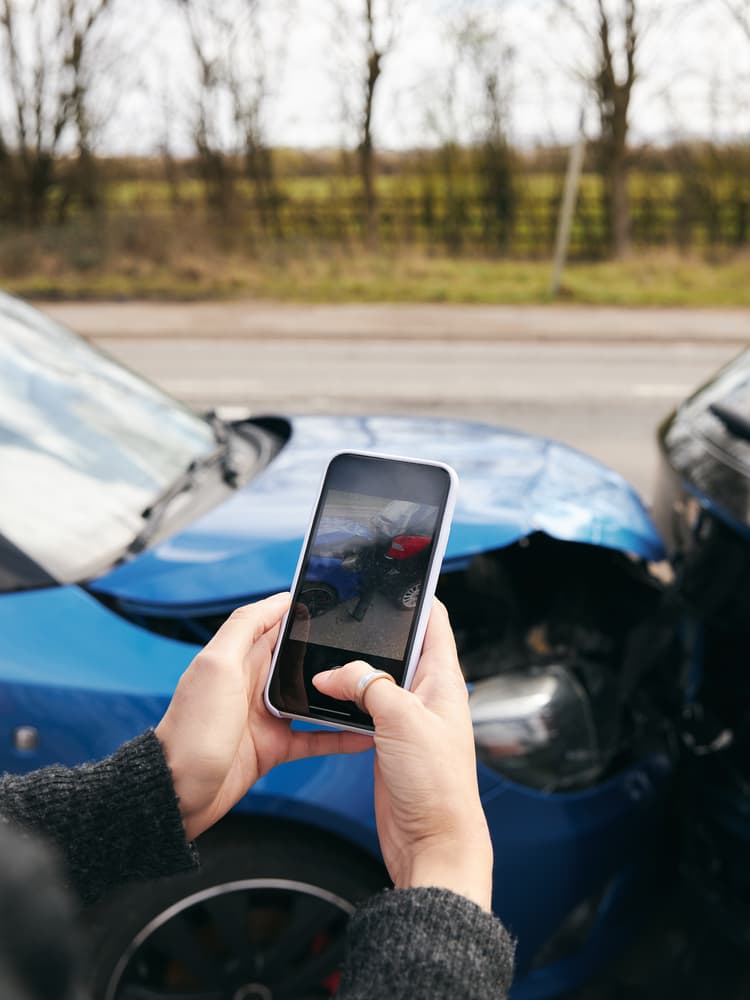 A close-up of a female driver taking photos of a road traffic accident on her mobile phone for an insurance claim.