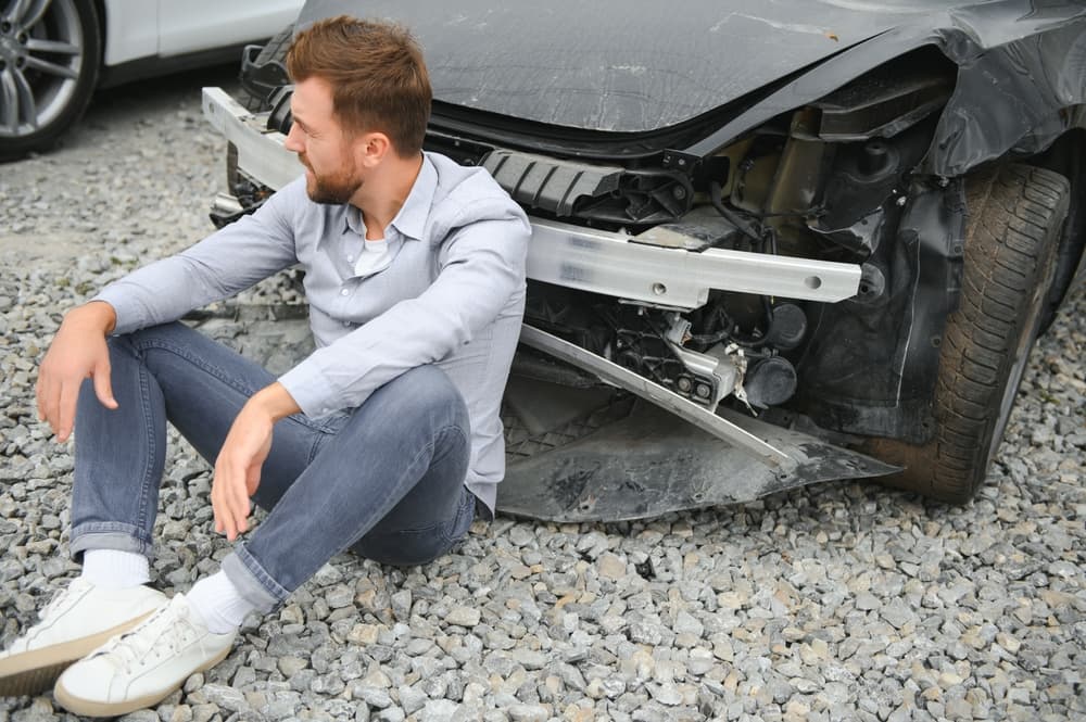 Man standing next to damaged car, reflecting on the aftermath of a car accident and expressing regret.