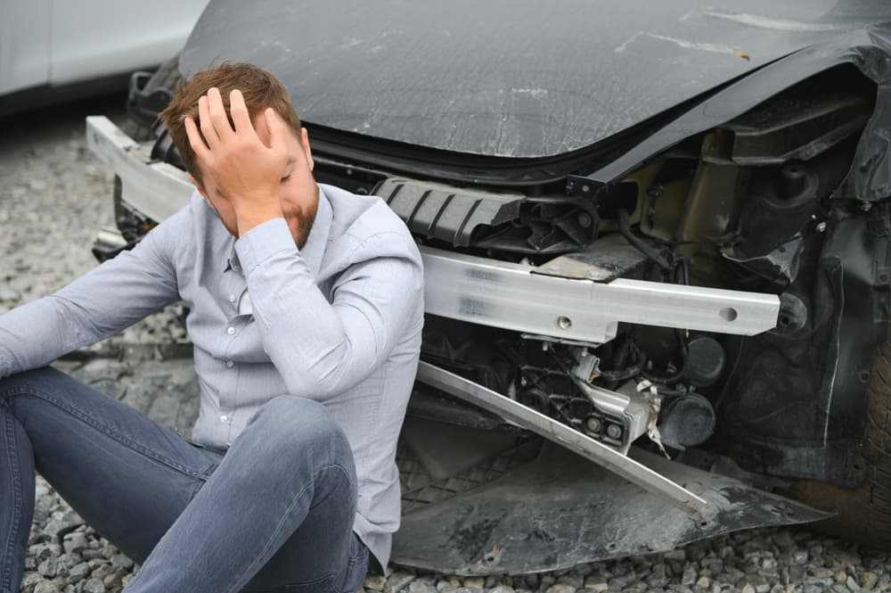A man near a damaged car, expressing frustration and concern over the extent of the damage, realizing the car is irreparable.