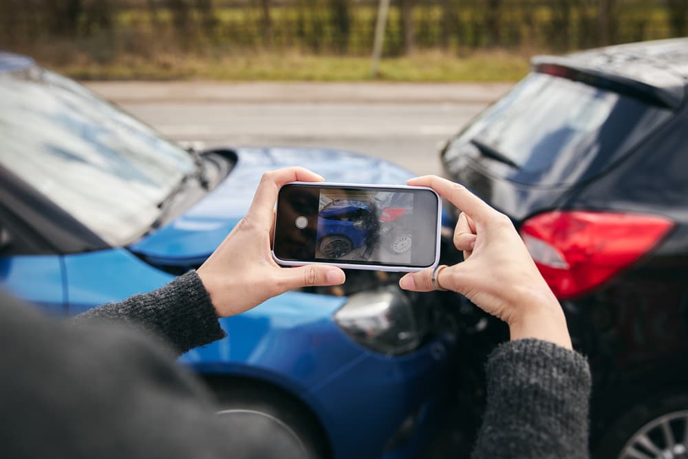 Close-up of a female driver using a mobile phone to photograph a road traffic accident for an insurance claim.