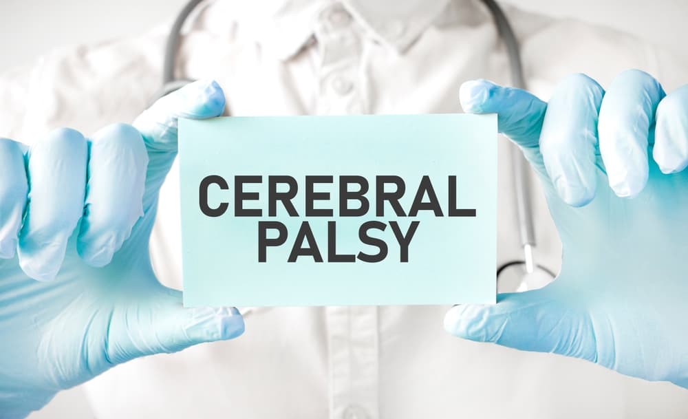 A doctor holding a card in their hands, pointing to the words "CEREBRAL PALSY," highlighting the condition for awareness or discussion.