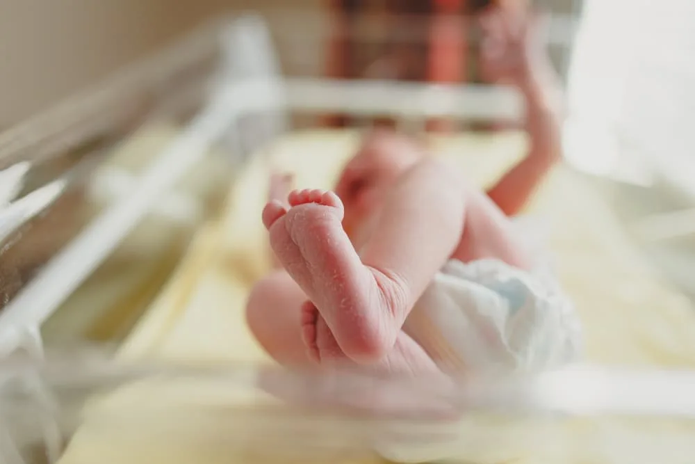 A newborn resting in a transparent crib at a maternity hospital, surrounded by a calm, sterile environment, with soft lighting highlighting the baby's peaceful sleep and the hospital setting.