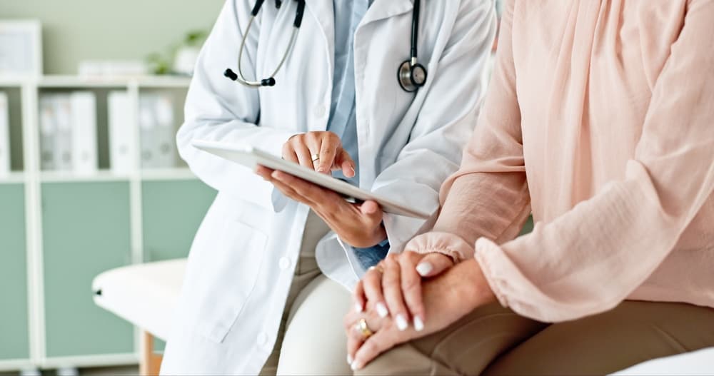 In a clinic, a doctor holds a tablet while consulting with a patient, providing medical services and assistance in a hospital setting.







