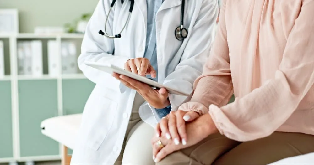 In a clinic, a doctor holds a tablet while consulting with a patient, providing medical services and assistance in a hospital setting.