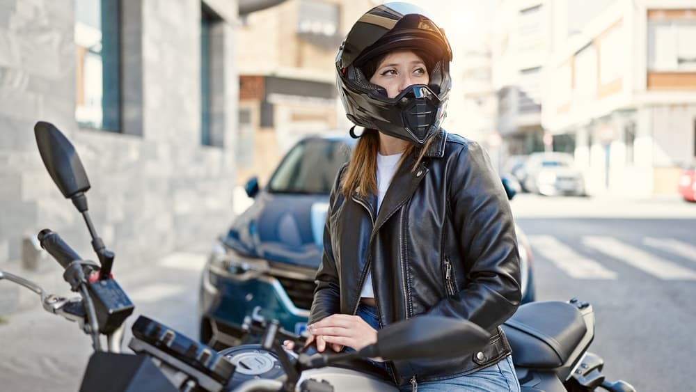 A young blonde woman wearing a motorcycle helmet stands on the street.