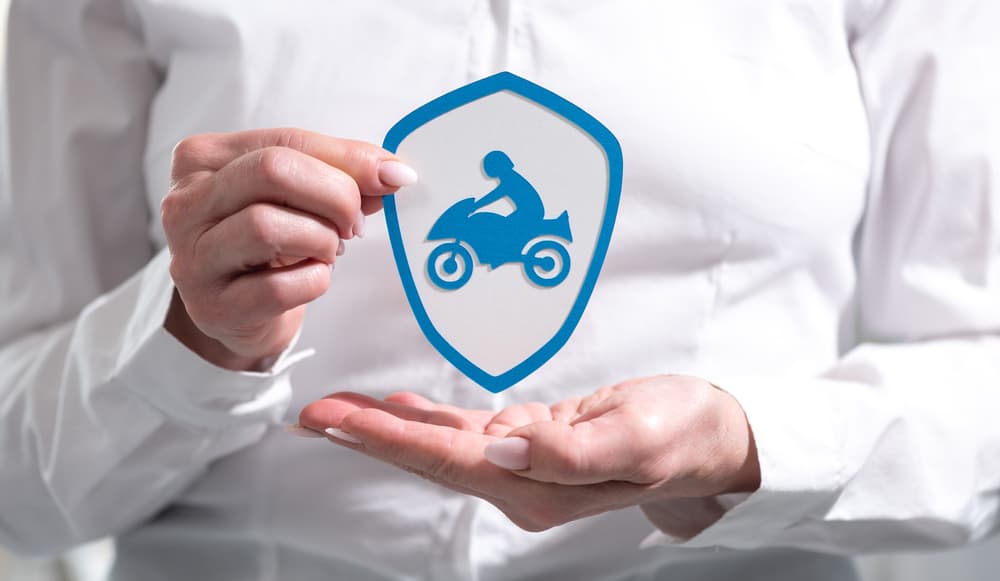 A female hand holding a paper shield, symbolizing the concept of motorbike insurance and protection.