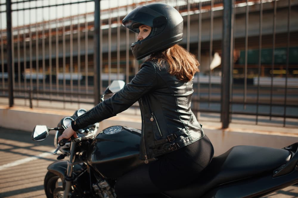 A cute young brunette woman standing next to a motorcycle.