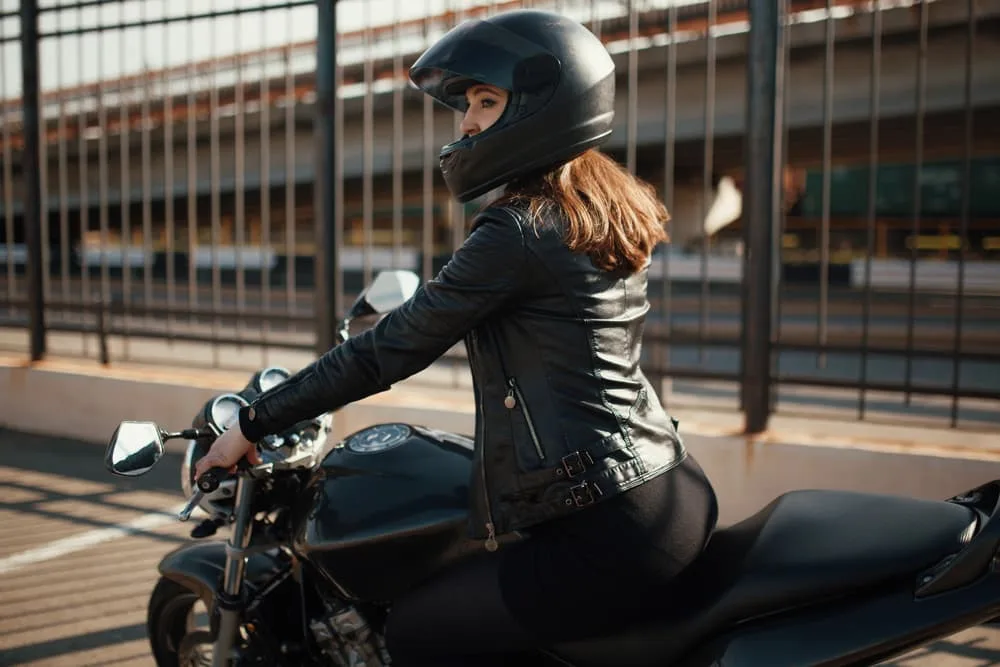 A cute young brunette woman standing next to a motorcycle.