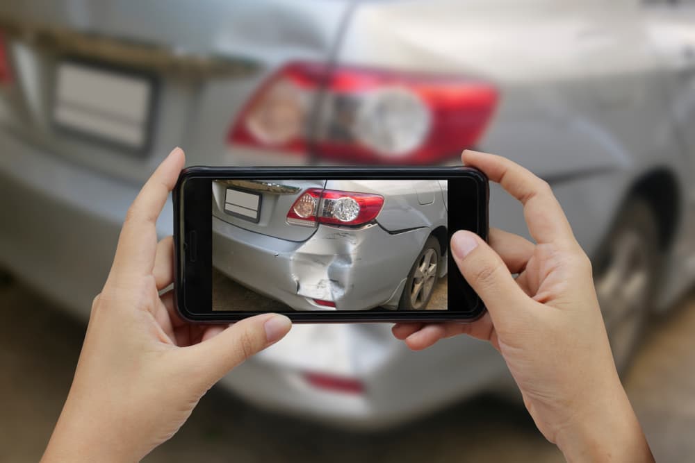 A close-up of a woman's hand holding a smartphone, taking photos at the scene of a car crash.