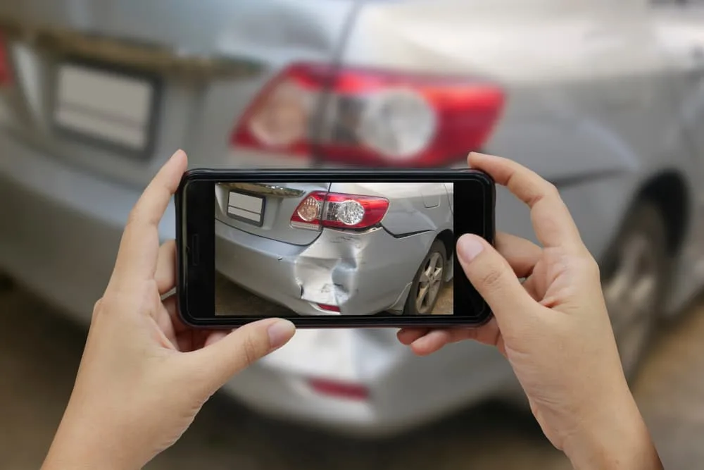 A close-up of a woman's hand holding a smartphone, taking photos at the scene of a car crash.