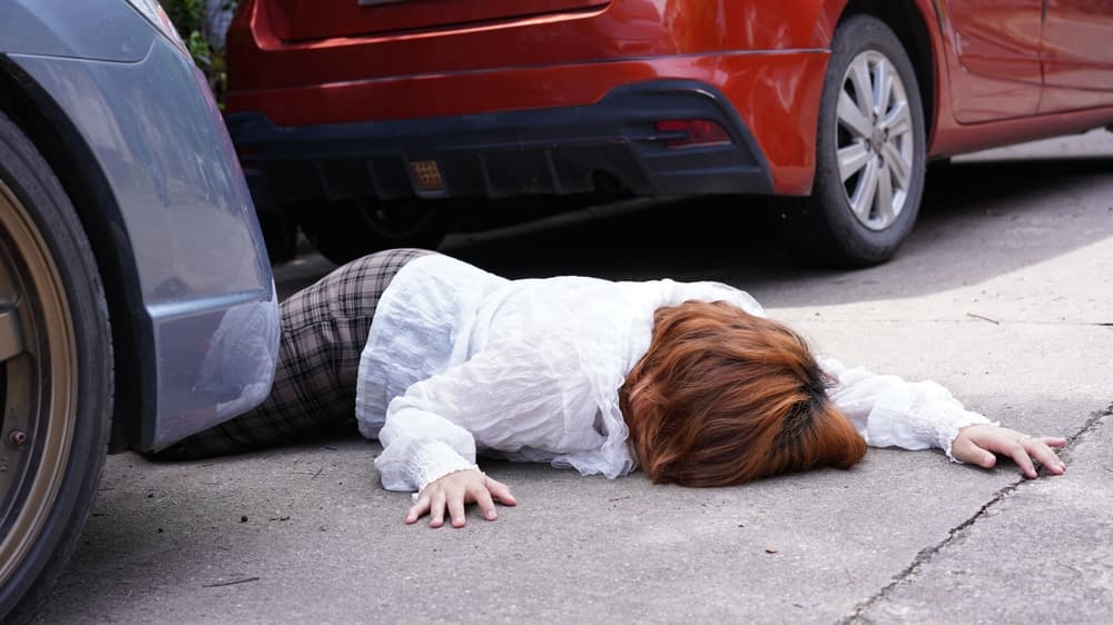 A tragic scene of a fatal road accident where a female pedestrian lies motionless on the street after being hit by a silver car, symbolizing the severity of vehicular accidents and the devastating consequences of such collisions.