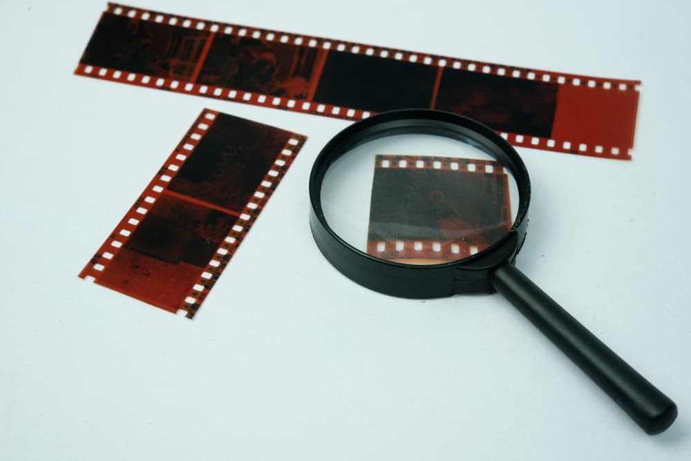 Magnifying glass placed over a strip of negative film, symbolizing the concept of finding evidence in a crime investigation.