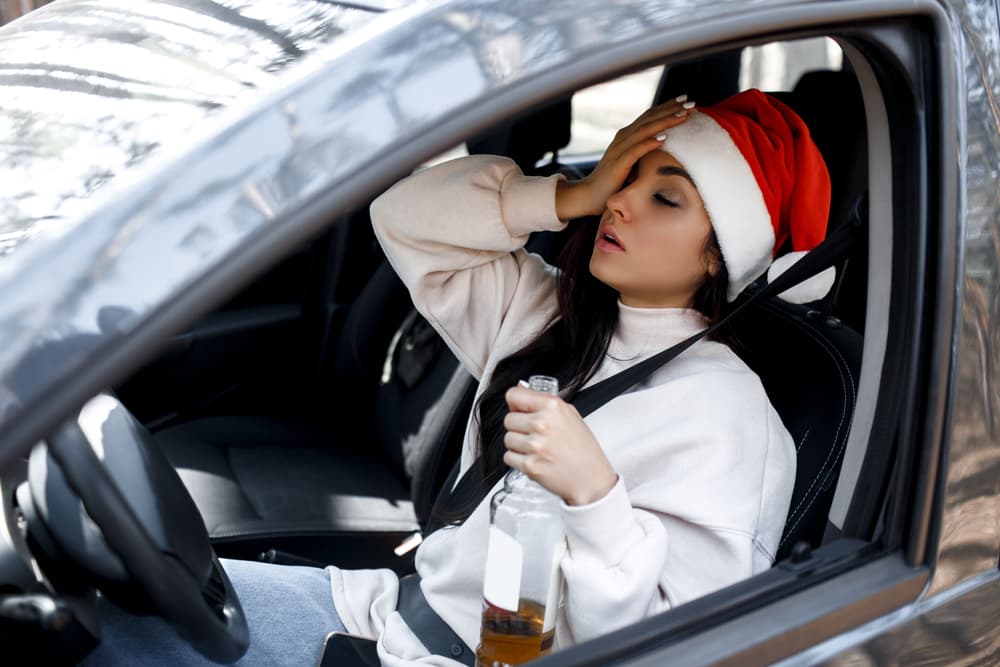 Drunk woman sitting in the driver's seat with a drink in hand, highlighting the dangers of drinking and driving on New Year's Eve. A reminder that alcohol and driving don't mix, especially during holiday celebrations.