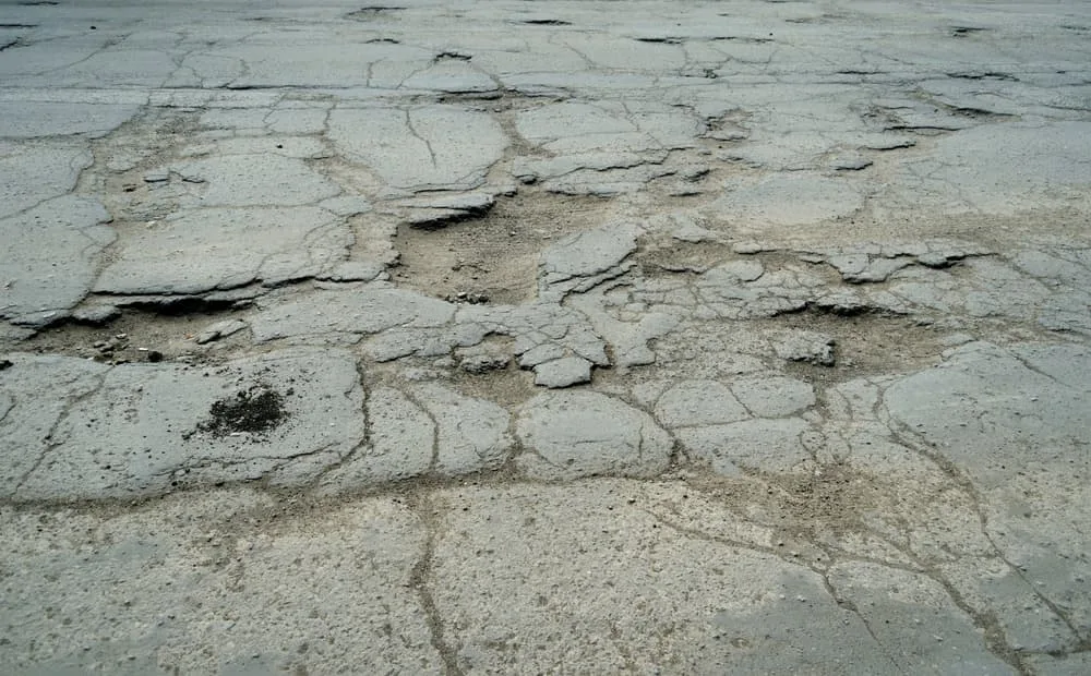 View from above of damaged road with pits and scattered stones on the asphalt, showing poor road conditions in need of repair. Concept of road construction and maintenance.