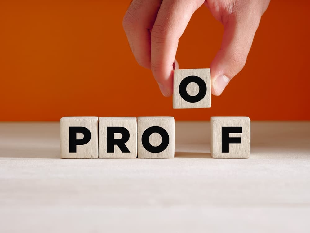 Hand placing a wooden cube with the word 'proof' on a surface. Concept of finding proof, evidence, or verifying something.