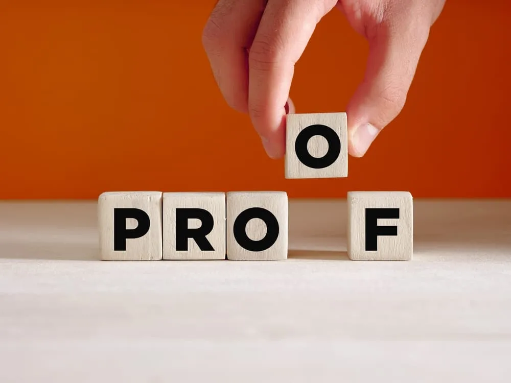 Hand placing a wooden cube with the word 'proof' on a surface. Concept of finding proof, evidence, or verifying something.