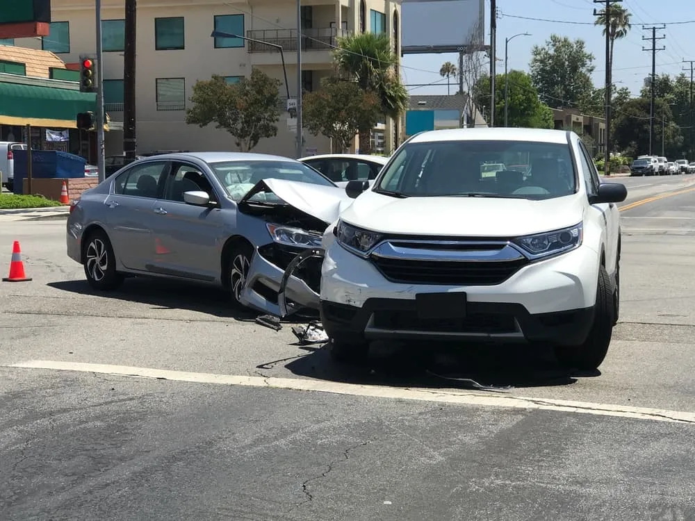 Two modern vehicles involved in a traffic accident are shown stopped in an intersection during the day.