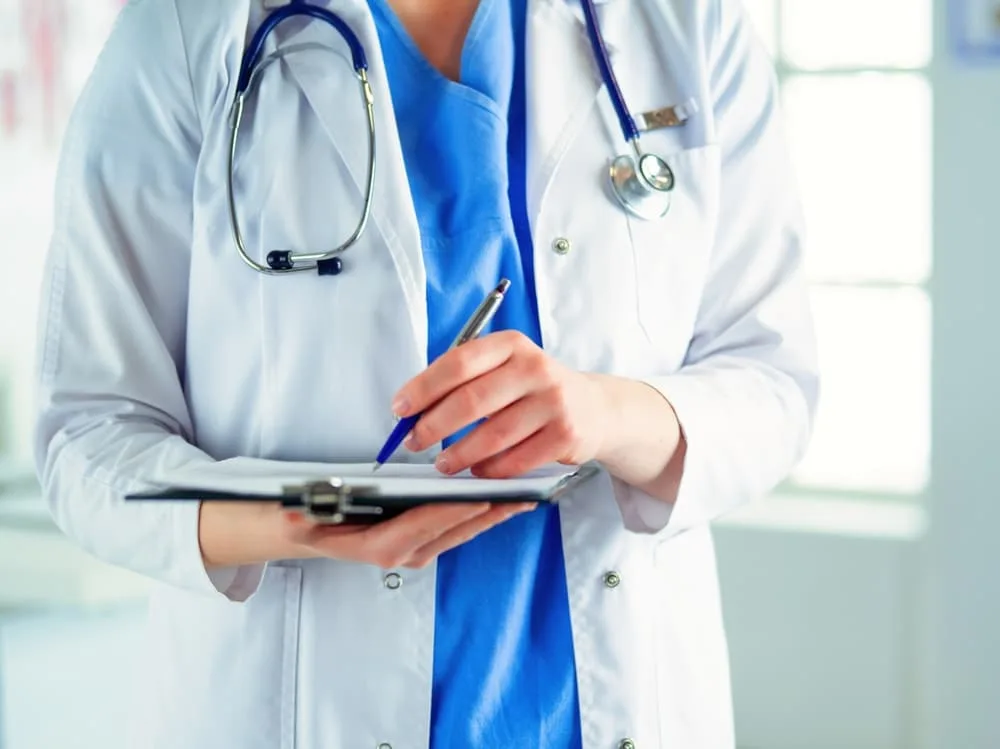 A female doctor filling up medical form at clipboard while standing straight in hospital Doctor with a stethoscope, holding a note.