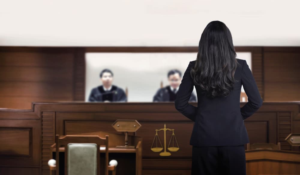 Attorney woman on courtroom talking to magistrate in court box defending medical malpractice case.