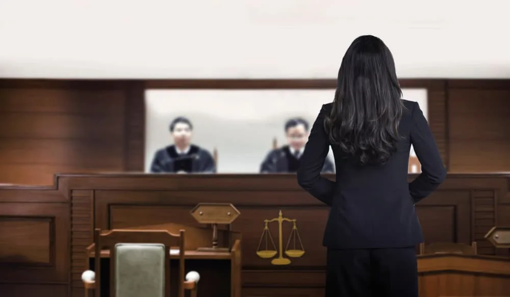 Attorney woman on courtroom talking to magistrate in court box defending medical malpractice case.