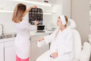 A doctor in a white coat shows and explains a set of medical scans to a patient sitting in a clinic room.