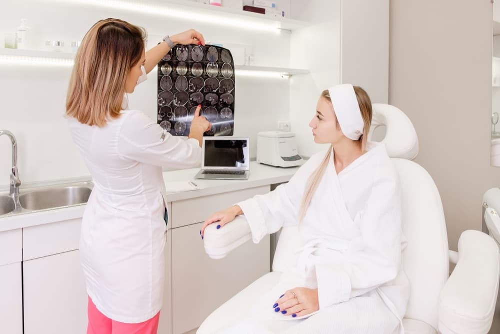 A doctor in a white coat shows and explains a set of medical scans to a patient sitting in a clinic room.