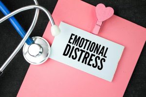A stethoscope rests on a pink clipboard holding a card labeled "EMOTIONAL DISTRESS" with a pink heart-shaped clip.