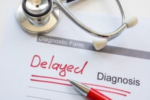 A stethoscope and pen rest on a diagnosis form with the word "Delayed" written in red next to the printed word "Diagnosis.