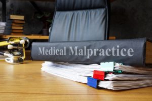 A binder labeled "Medical Malpractice" rests on a desk beside a stack of documents with colorful clips and a stethoscope.