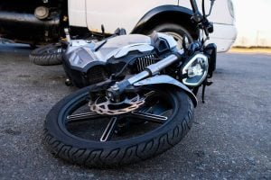 A motorcycle is lying on its side on the pavement next to a white vehicle, suggesting a recent accident or collision.
