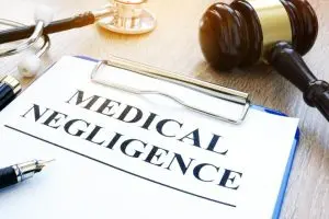 A clipboard with a document titled "Medical Negligence" next to a gavel, a stethoscope, and a pen on a wooden desk.