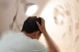 A person holding their head with both hands, surrounded by a blurred, swirling background suggesting dizziness or disorientation.