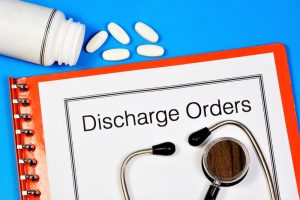 A stethoscope and white pills are placed on a red notebook with a cover labeled "Discharge Orders" against a blue background.