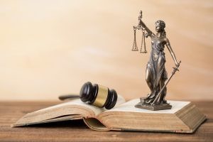 A gavel and Lady Justice statue are placed on an open book on a wooden surface.