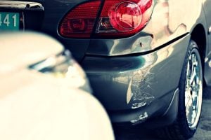 Close-up of two cars after a minor collision, with visible scratches and damage on the rear bumper of a dark car.