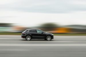 A black car driving quickly on a road, with a motion blur effect in the background.
