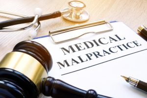 A clipboard labeled "Medical Malpractice" is shown next to a stethoscope, gavel, and fountain pen on a wooden surface.