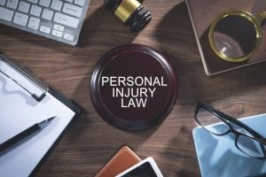 A wooden desk with a gavel, clipboard, keyboard, glasses, phone, and a plaque reading "PERSONAL INJURY LAW" in the center.