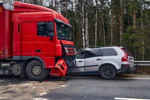 A red semi-truck and a silver SUV are involved in a head-on collision on a roadway near a forested area.