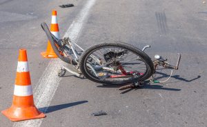 A damaged bicycle lies on its side on an asphalt road, surrounded by three orange and white traffic cones.