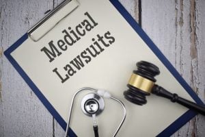 A clipboard with a paper labeled "Medical Lawsuits," beside a stethoscope and a judge's gavel on a wooden surface.