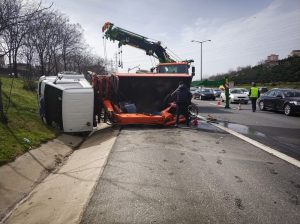 Overturned vehicles and a damaged truck on a highway accident scene; a crane and emergency workers are on site, with traffic partially blocked.
