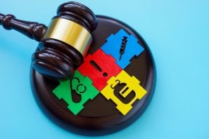 A judge's gavel rests on a puzzle of colorful pieces featuring healthcare symbols, including a stethoscope, syringe, and pill, against a blue background.