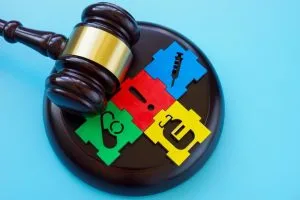 A judge's gavel rests on a puzzle of colorful pieces featuring healthcare symbols, including a stethoscope, syringe, and pill, against a blue background.
