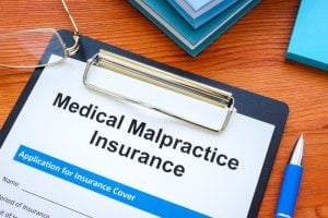A clipboard with a “Medical Malpractice Insurance” form on a desk, next to a pair of glasses and stacked books.